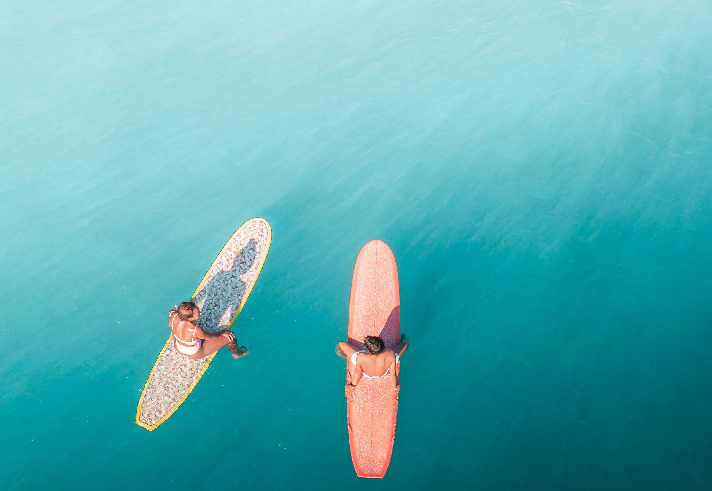Vue aérienne de deux vacanciers assis sur leurs planches de surf dans une eau turquoise